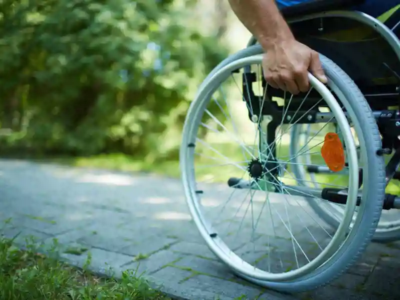Close-up of male hand on wheel of wheelchair during walk in park